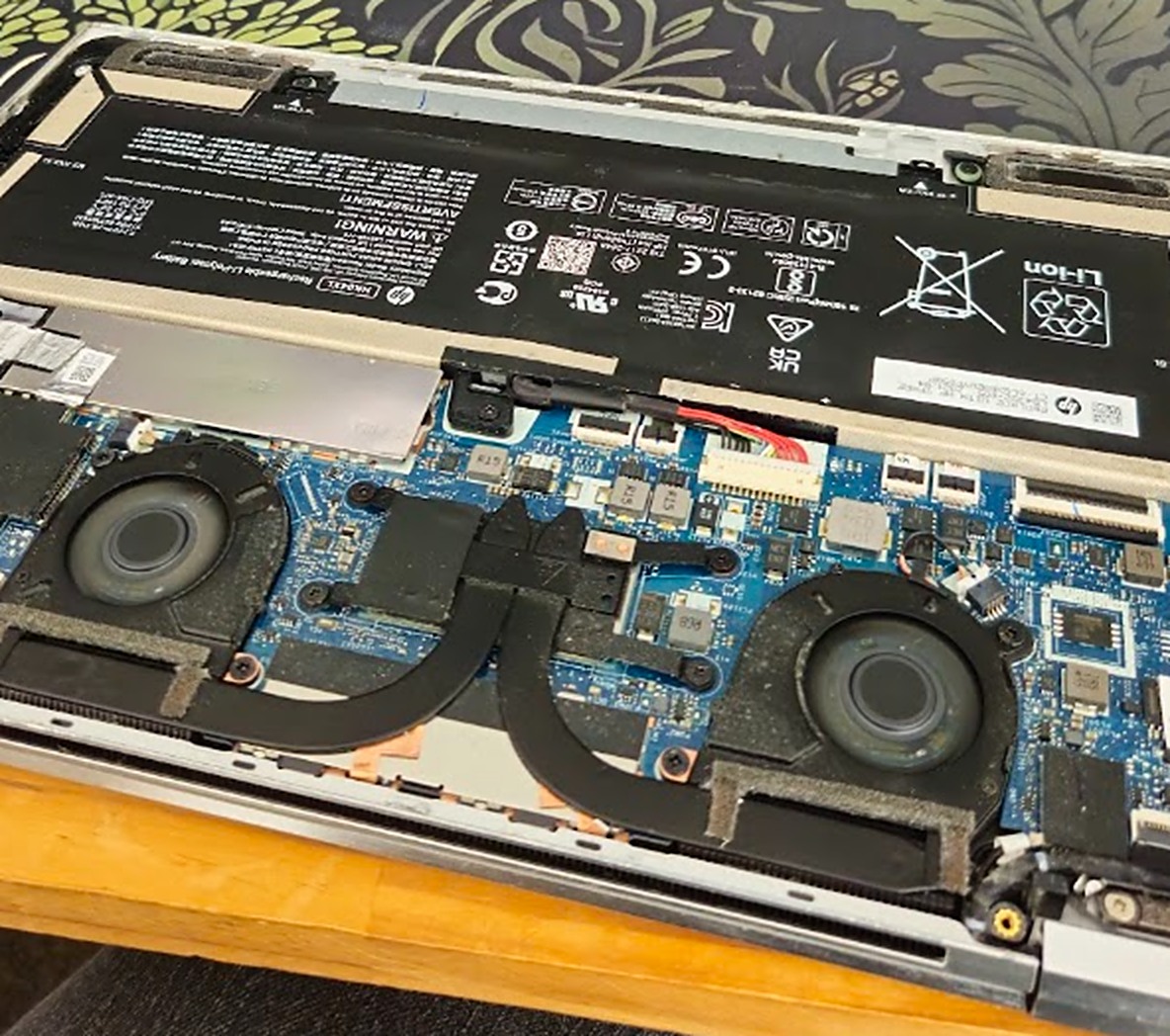 The laptop with its bottom cover off, showing the battery, twin fans, heat pipe, and motherboard
