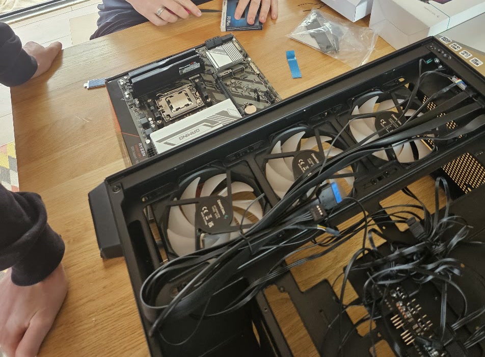 A PC build in progress: an AMD motherboard with RAM fitted beside an open case with three fans and a mess of cables