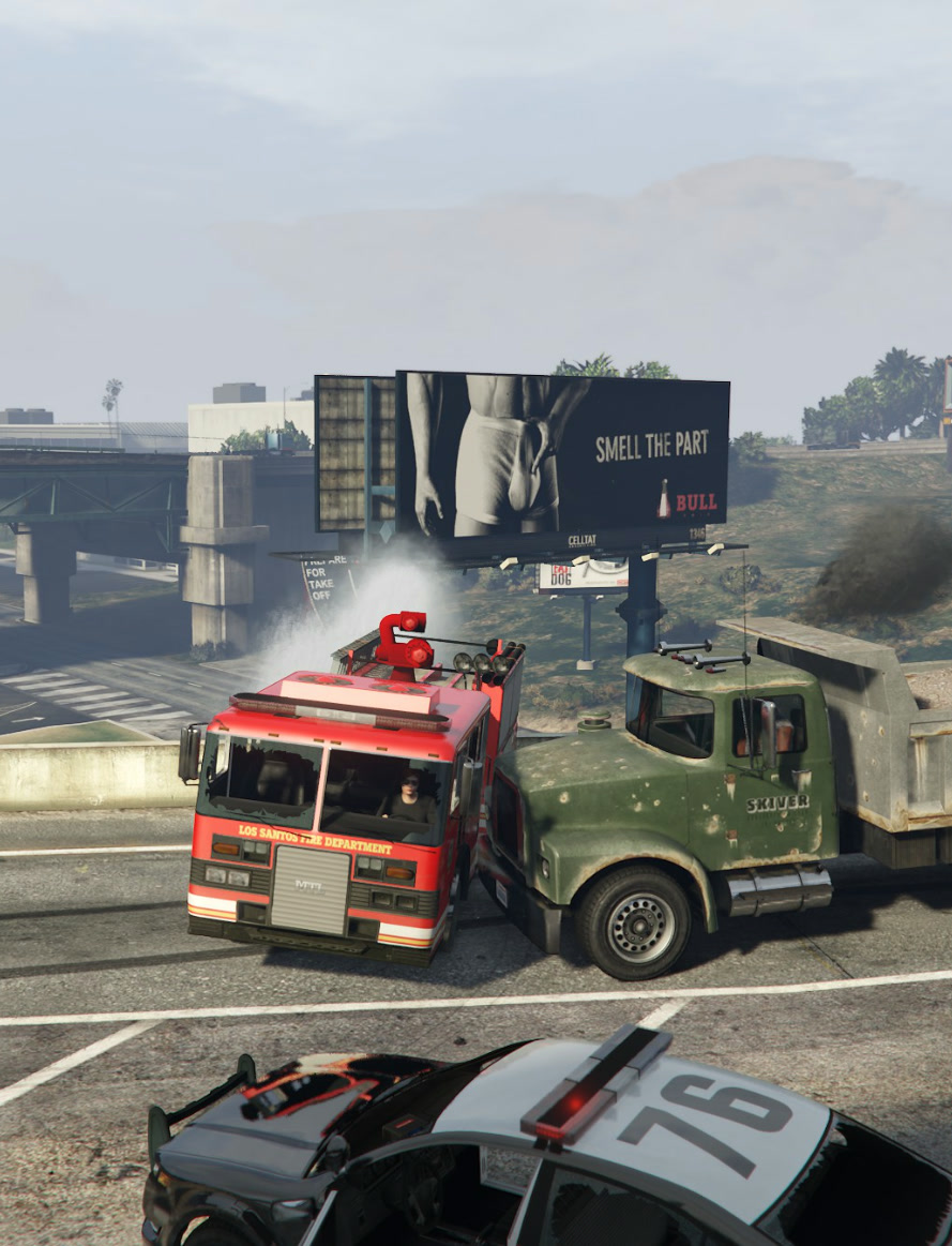 GTA V: a fire truck and a dump truck locked together on the freeway under a Bull cologne billboard, a police car in the foreground
